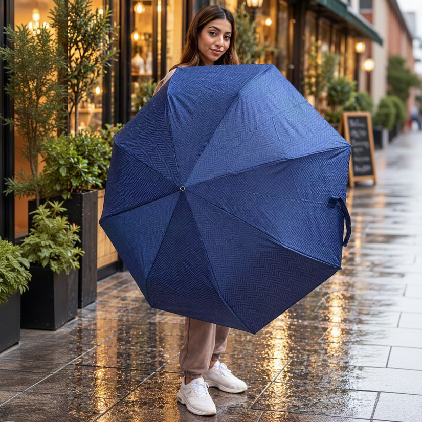 Woman holding open a navy herringbone folding umbrella on a wet street