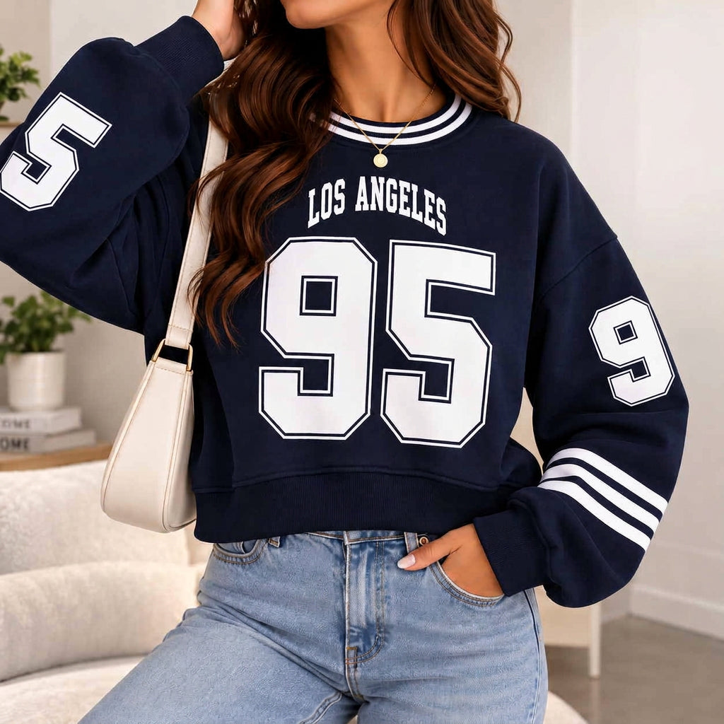 Woman in a cropped navy Los Angeles 95 varsity sweatshirt with white striped sleeves