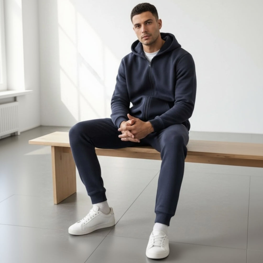 Man sitting on a wooden bench wearing a navy tracksuit and white sneakers