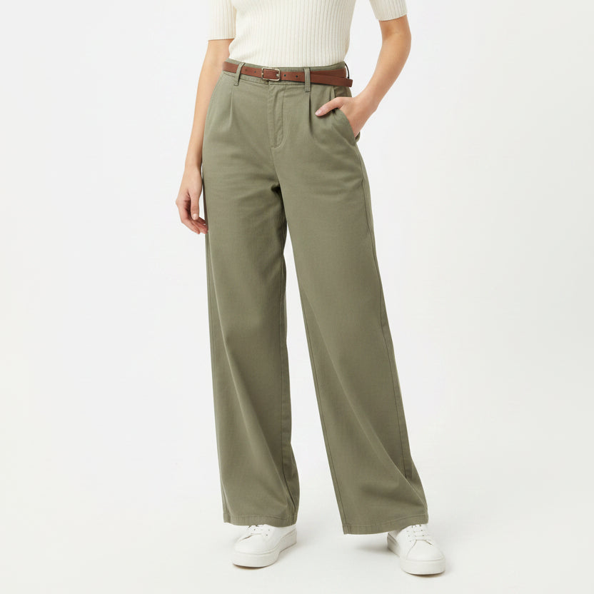 Person wearing olive green pants with a white top and white shoes on a white background