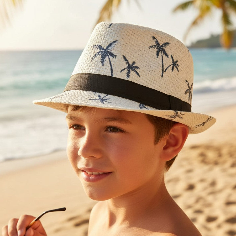 Boy wearing a white straw fedora sun hat with a navy palm tree print and black band