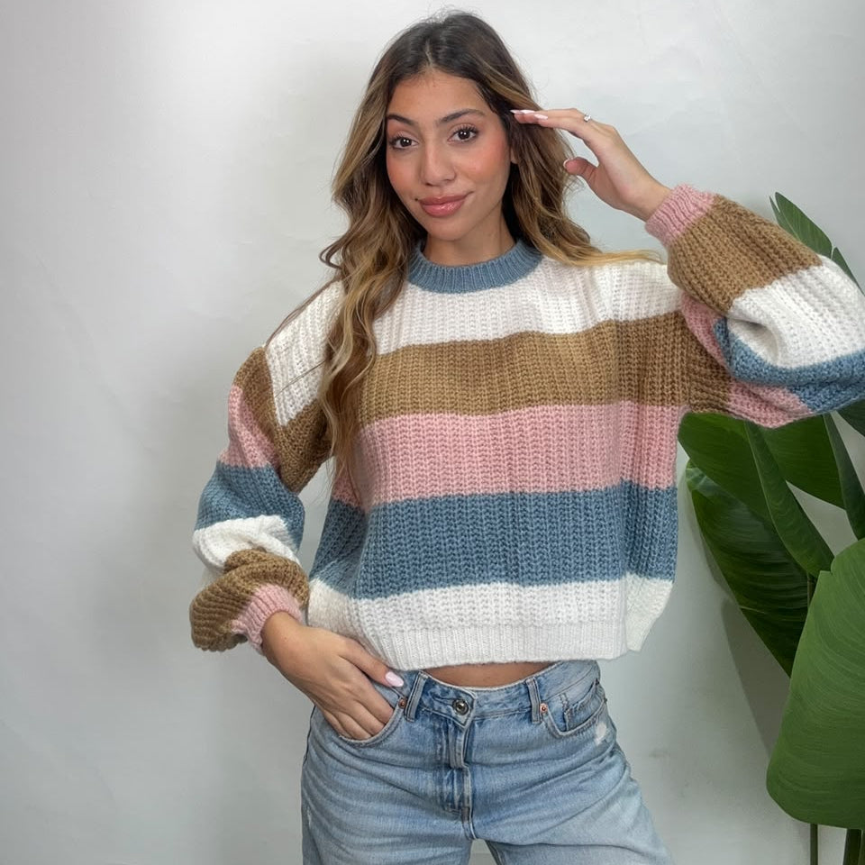 Woman in a cropped pastel striped knit sweater with blue sleeves, hand in her hair