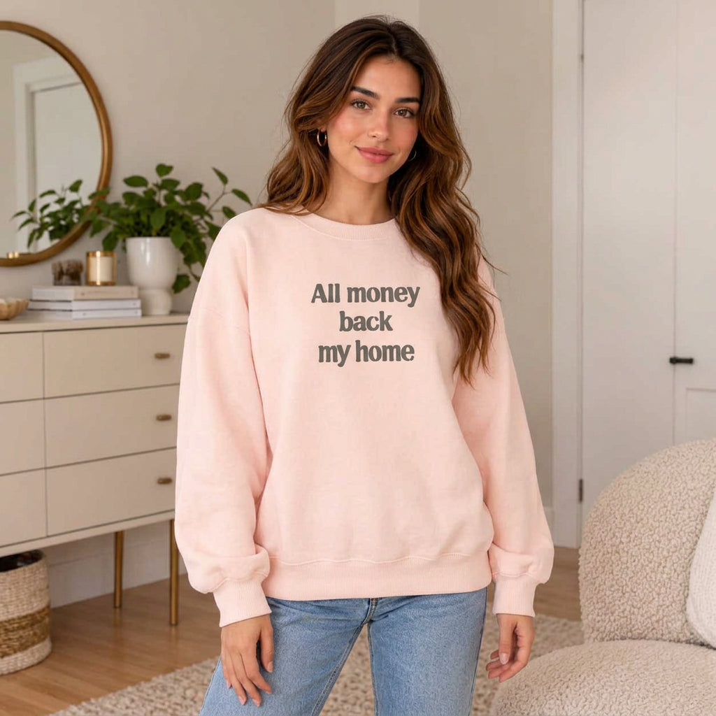 Woman in a pink sweatshirt with an All Money Back My Home slogan print and light blue jeans