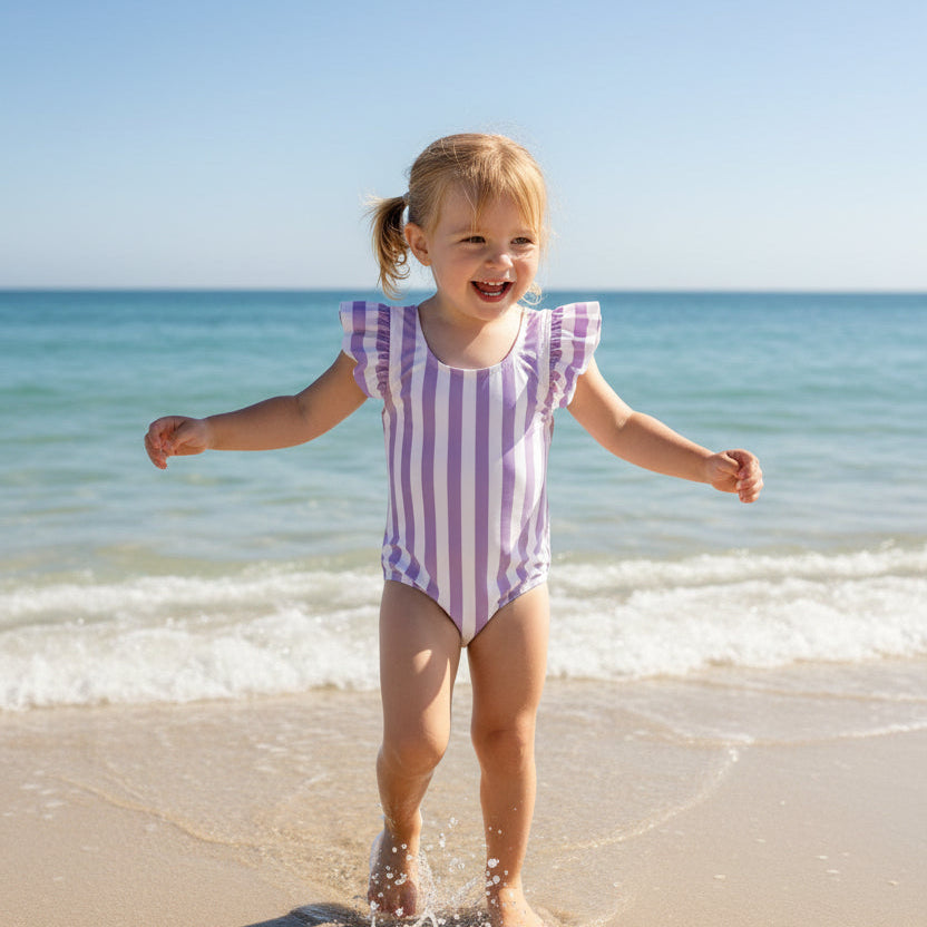 Girl wearing a purple striped onepiece swimsuit with ruffled cap sleeves on the beach