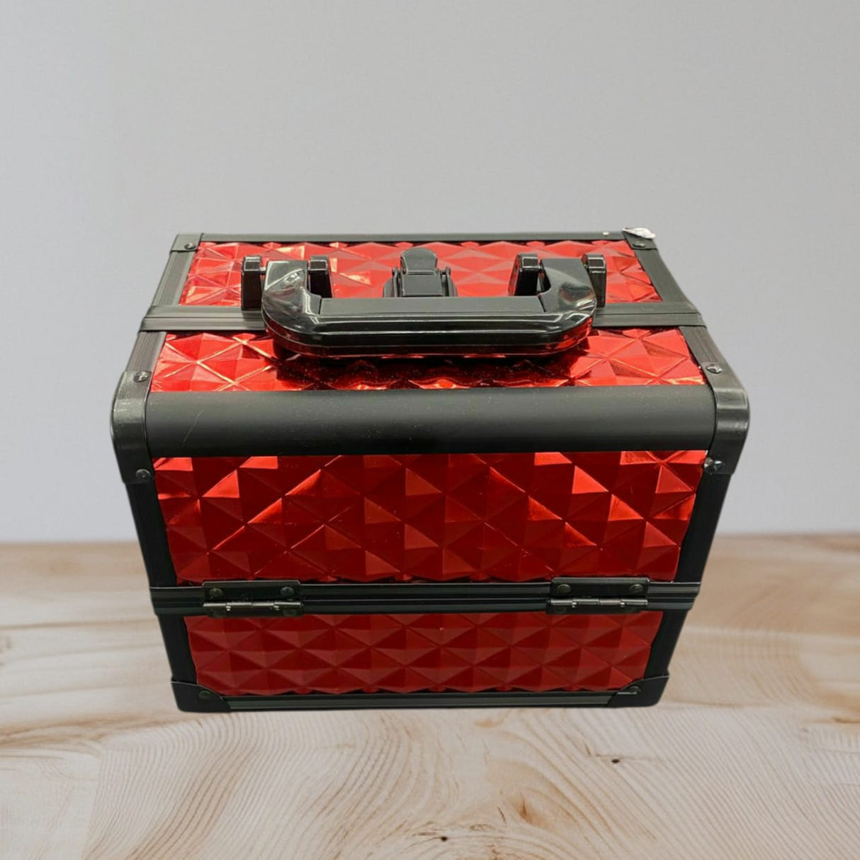 Glossy red studded aluminium case closed with black edge rails and a black carry handle