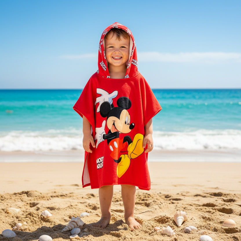 Boy on the beach wearing a red Mickey Mouse poncho towel with a waving Mickey print