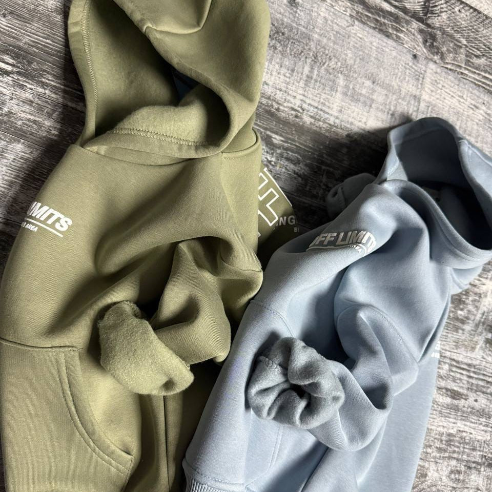 Sage green and light blue hoodies side by side on a wooden floor