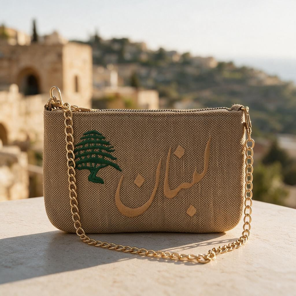 Jute look mini bag with tone on tone Arabic lettering and a cedar, gold chain curled in front, hillside village behind