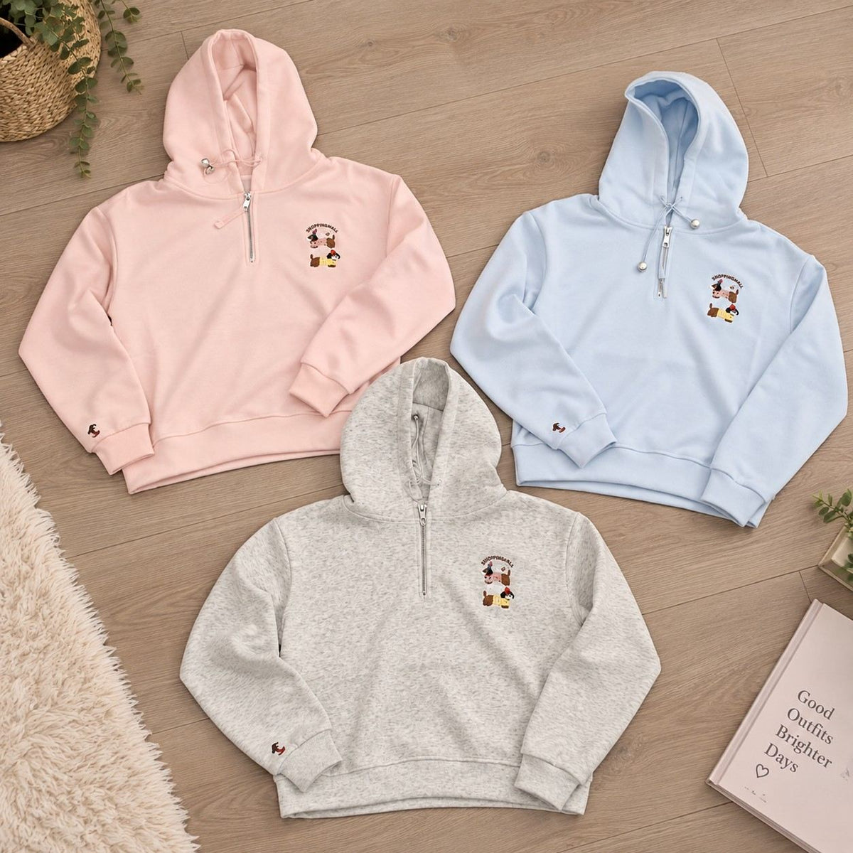 Grey, light blue and pink half zip hoodies laid out together on a wooden floor