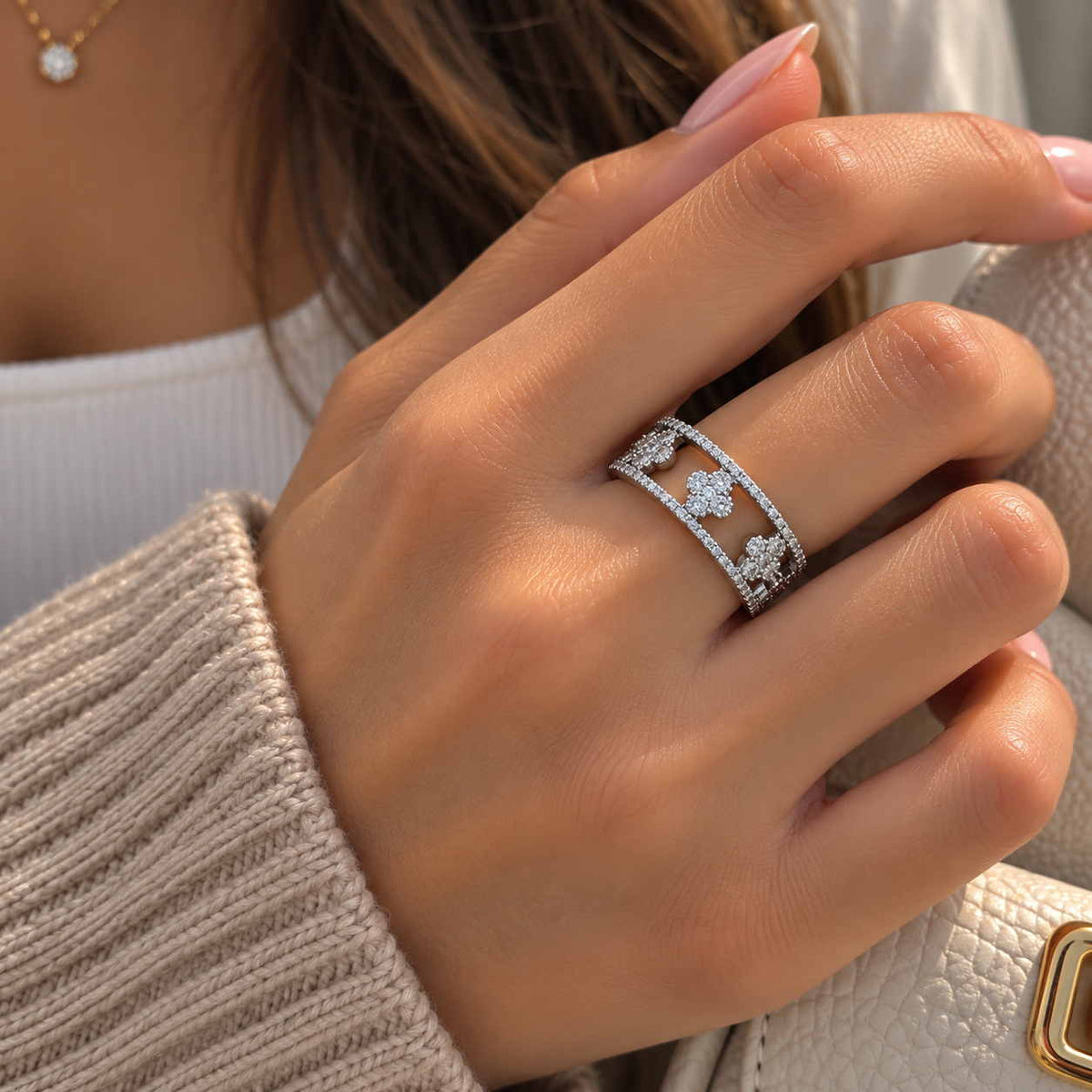 Hand wearing a wide silver openwork ring with crystal clovers, beside a beige knit sleeve