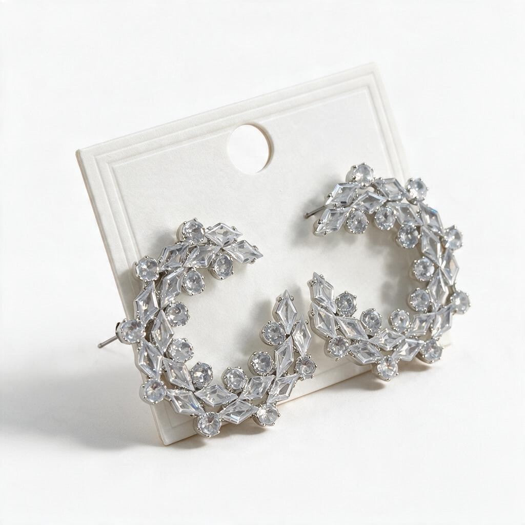 Pair of silver tone crystal wreath statement earrings resting on a white card