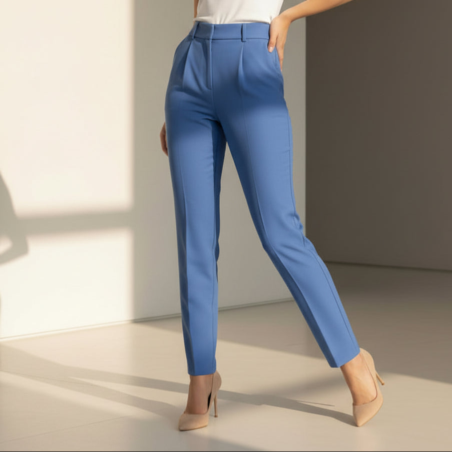 Woman wearing a white top and sky blue pants standing against a neutral wall