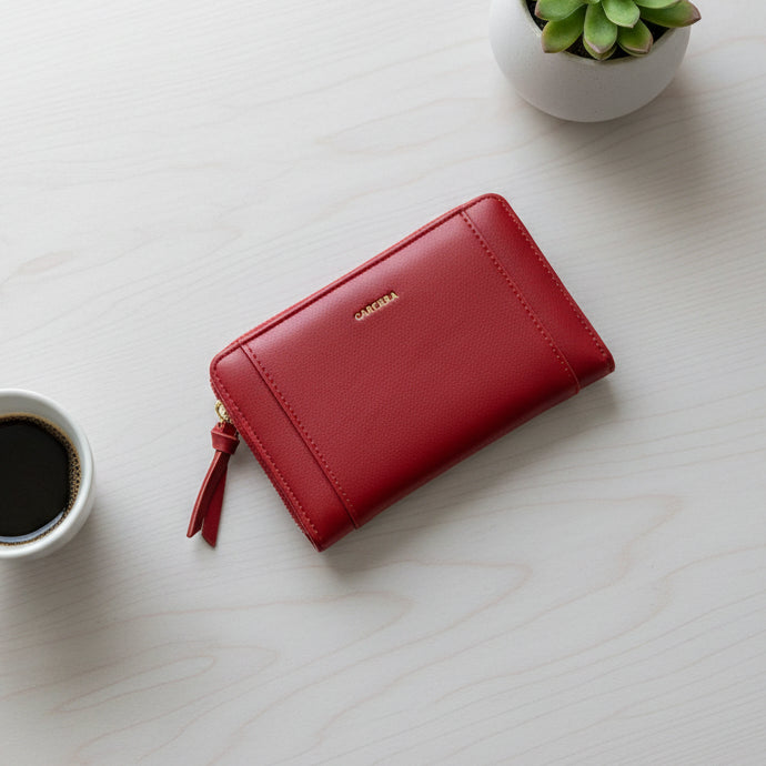 Red wallet on a light wooden surface next to a cup of coffee and a small plant