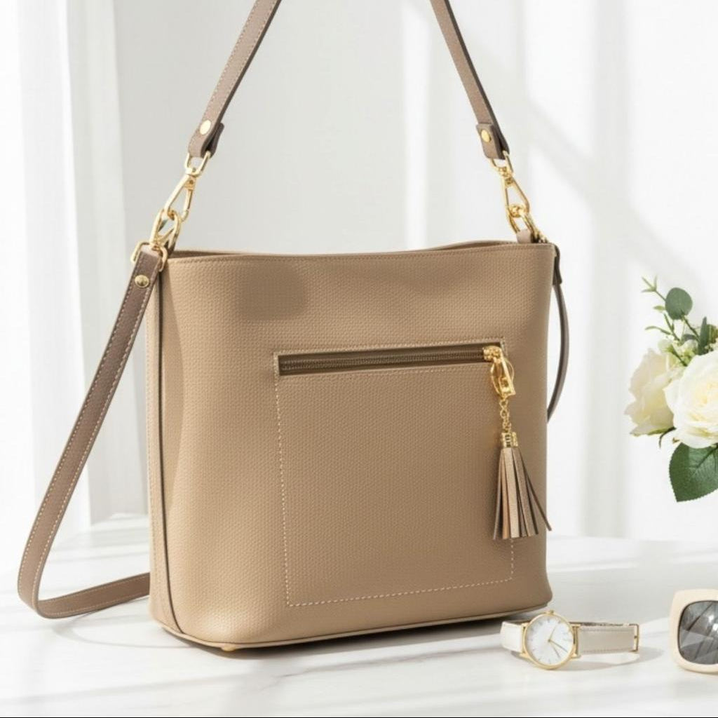 Beige bag at an angle showing the zip front pocket, gold clips and a gold tassel