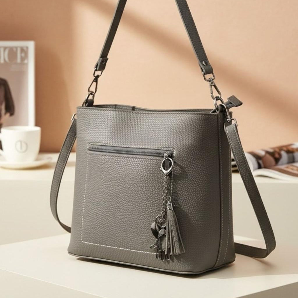 Grey shoulder bag seen from the side with its long adjustable strap and silver tassel
