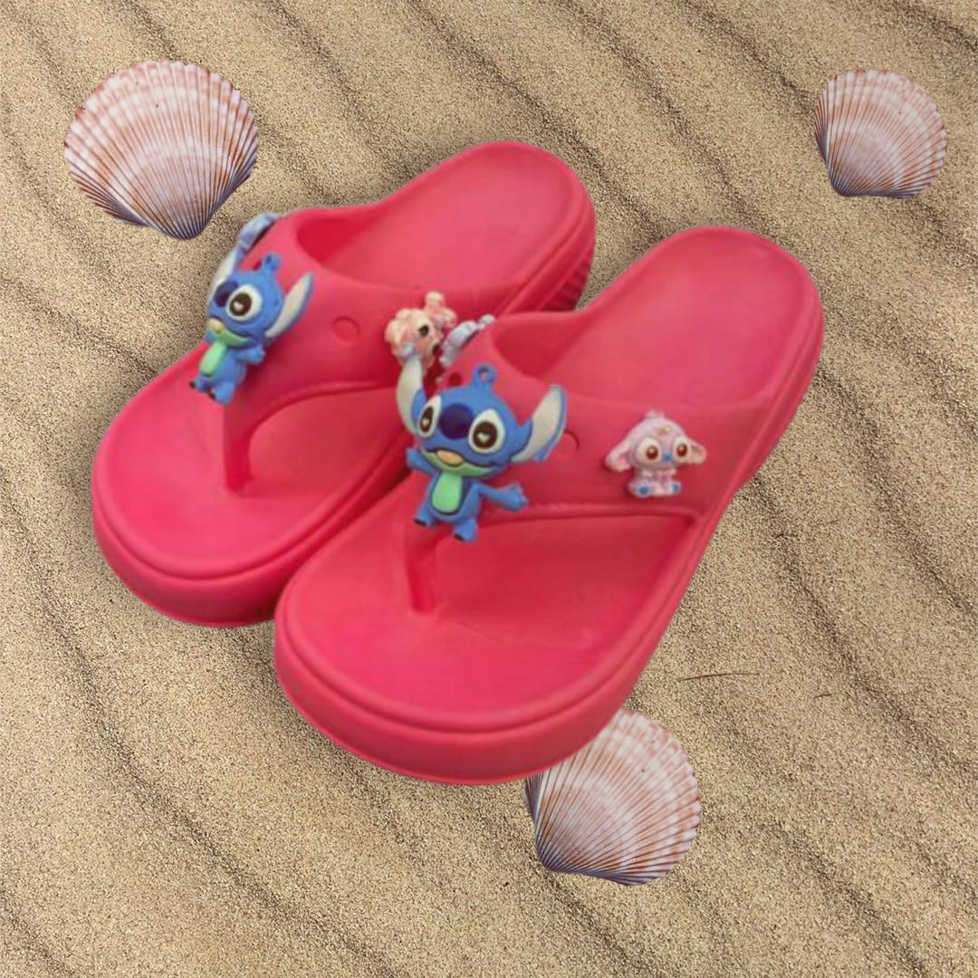 Pink cushioned flip flops with blue and pastel charms laid on rippled sand with shells
