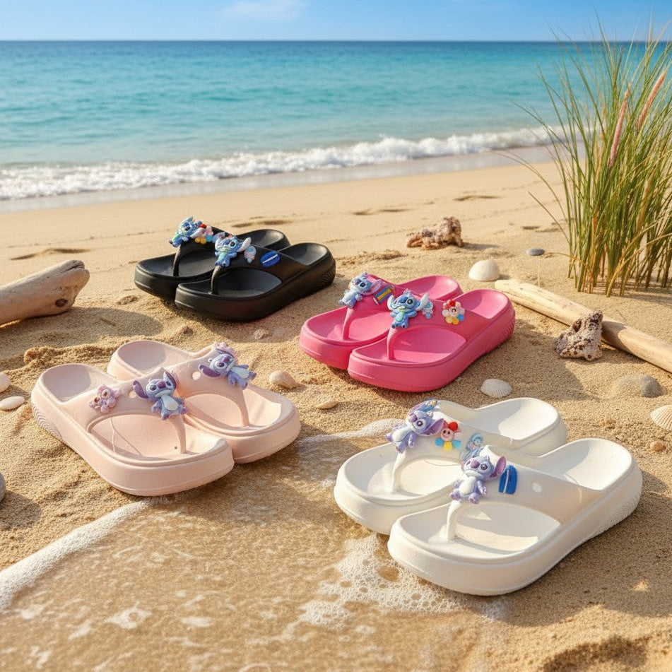 Four pairs of kids flip flops in black, pink, white and beige lined up on golden sand