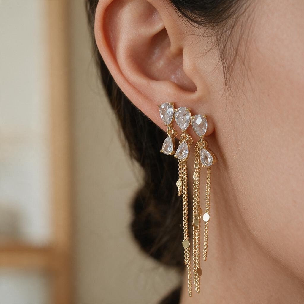 Gold chain tassel earring with clear pear cut crystals hanging from the earlobe