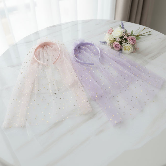 Pink and lilac headbands with long sparkling star print tulle veils spread across a round white table