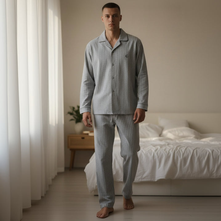 Man wearing striped pajamas standing in a bedroom with a bed and curtains.