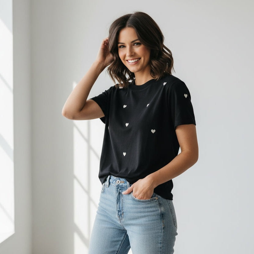 Woman wearing a black t-shirt with white heart patterns and light blue jeans indoors.