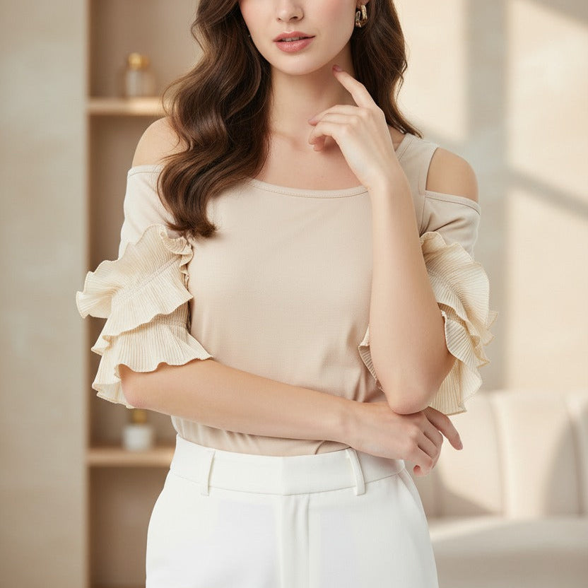 Woman wearing a beige off-shoulder top and white pants in a bright room.