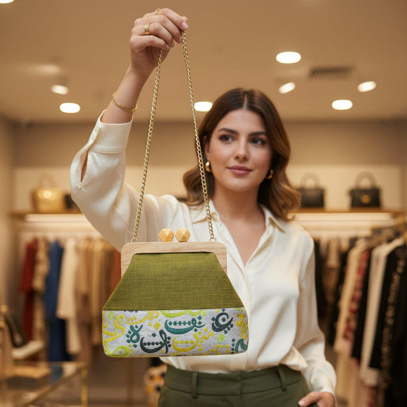 Green handbag with a colorful pattern and gold chain strap in a store setting.