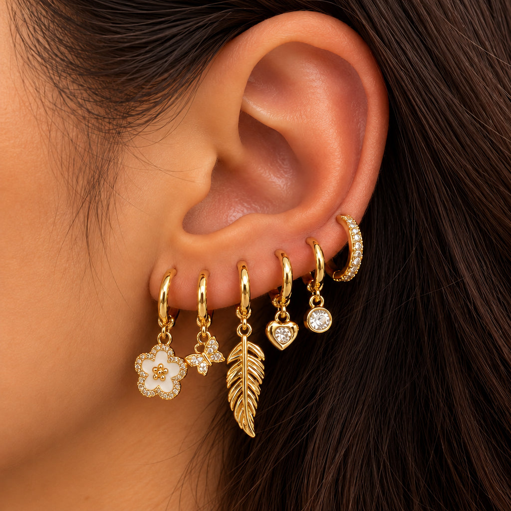 Ear stacked with gold huggies with a white flower, crystal butterfly, gold feather and heart charms