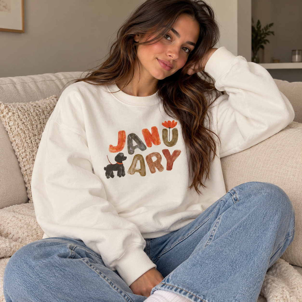 Woman in a white crew neck sweatshirt with colourful January lettering and a puppy print, sitting in jeans