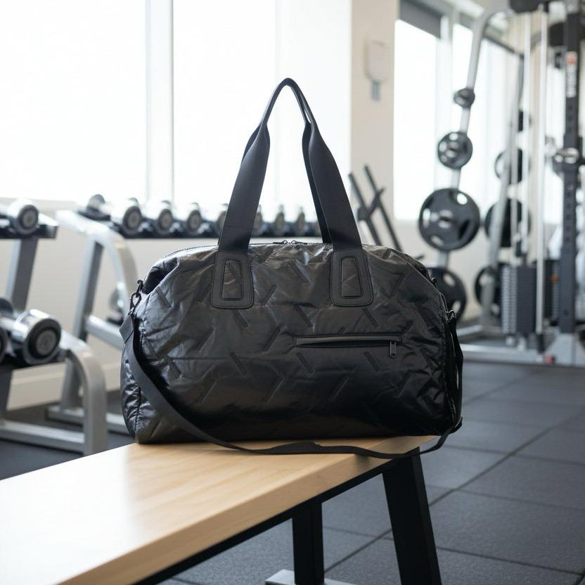 Black duffel bag on a wooden bench in a gym setting