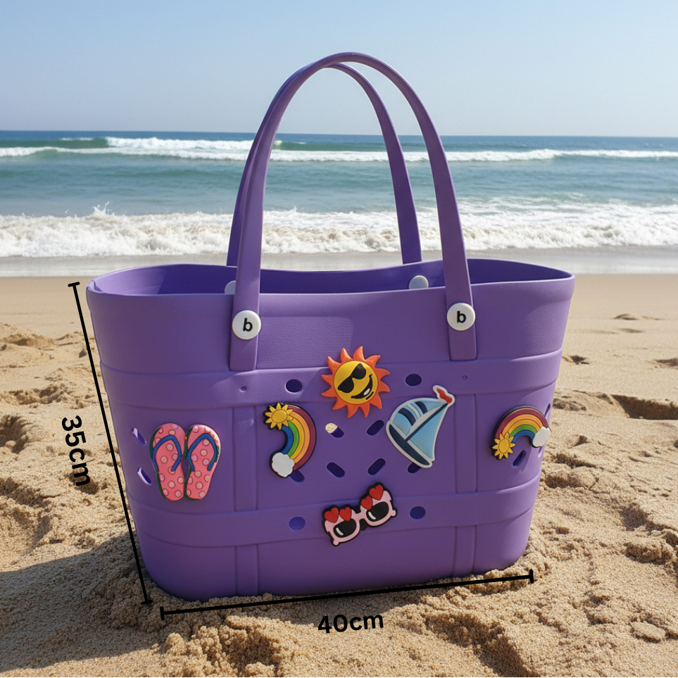 Purple beach bag with decorative stickers on a sandy beach with ocean waves in the background