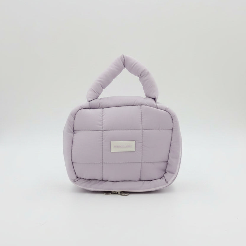 Purple quilted handbag with a visible brand label on a white surface, with pink and peach bags in the background.