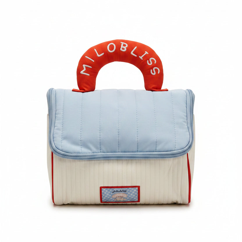 Baby bag with quilted top and red handle with 'Milo Bliss' branding, displayed in a store setting.