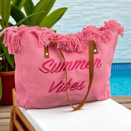 Pink beach bag with 'Summer Vibes' text on a chair by a poolside.