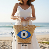 Woman holding a straw bag with an eye design on a beach, with measurements overlaid.