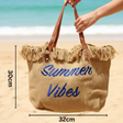 Beige tote bag with 'Summer Vibes' text on a beach, held by a hand.