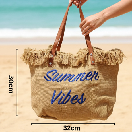 Beige tote bag with 'Summer Vibes' text on a beach, held by a hand.