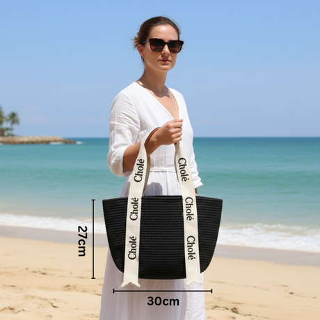 Woman holding a black straw bag with 'Chole' branding on a beach