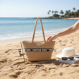 Woven bag with Christian Dior strap on a sandy beach, with a hand reaching towards it.