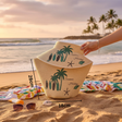 Woven bag with palm tree design on a sandy beach with ocean and palm trees in the background