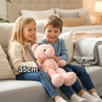 Baby pink seated teddy with a pale satin neck bow resting across two children's laps