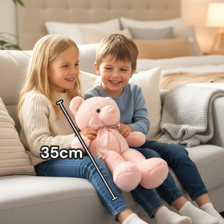 Baby pink seated teddy with a pale satin neck bow resting across two children's laps