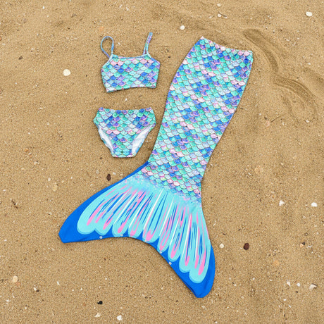 Three piece mermaid swimsuit with tail, top, and bottom flat lay on sand