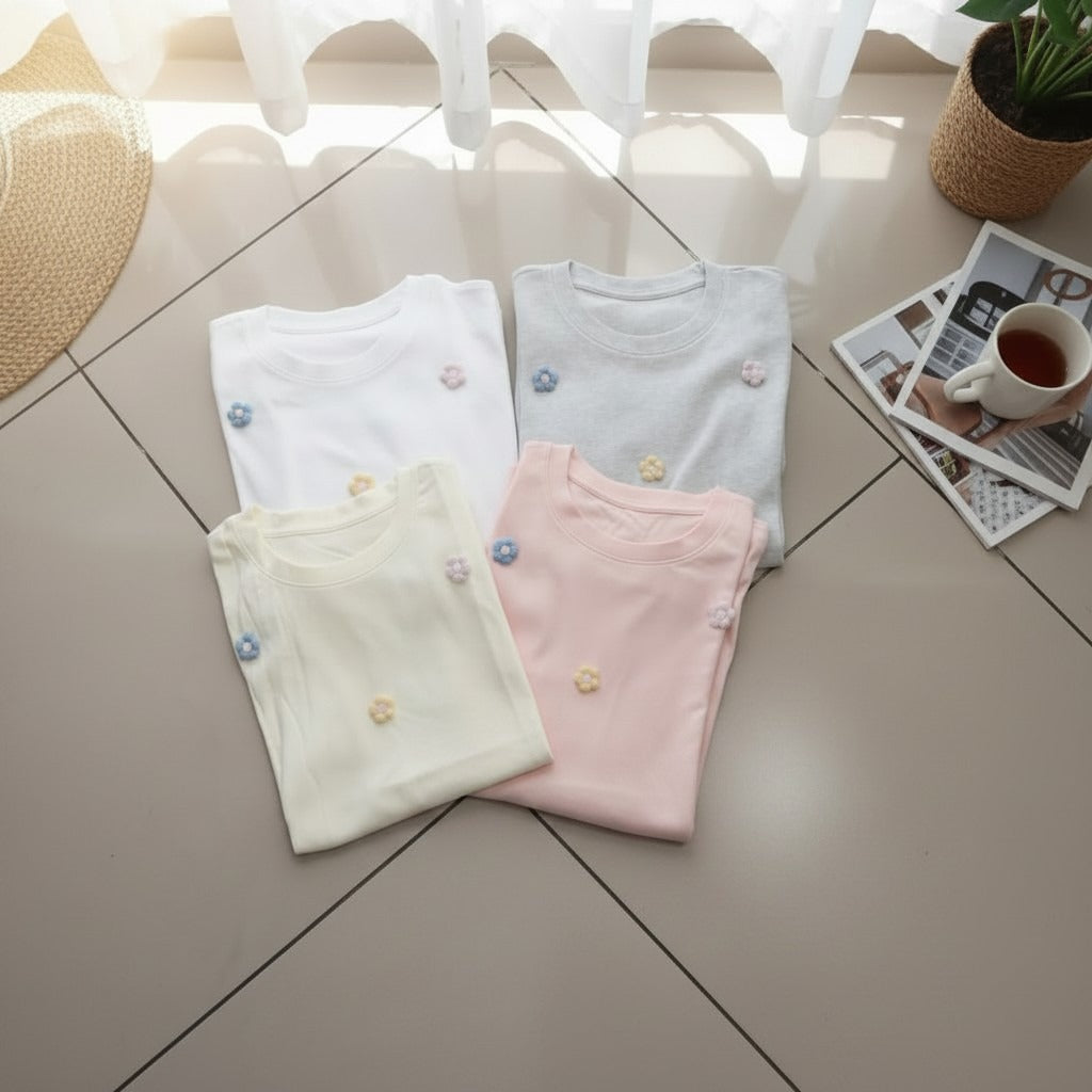 Four folded shirts in white, blue, yellow, and pink on a tiled floor with a cup of tea and photos in the background