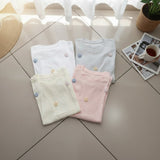 Four folded shirts in white, blue, yellow, and pink on a tiled floor with a cup of tea and photos in the background