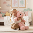 Baby pink teddy bear with a pale pink ribbon bow, held by a child on a rug