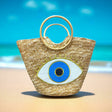 Woven straw bag with eye design on a beach