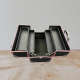 Pink aluminium makeup case open to show four grey lined trays with brush slots