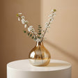 Honey amber glass vase with a rounded belly and short pinched neck on a white plinth