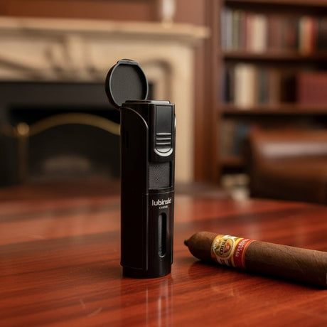 Black lighter with branding on a wooden surface next to a cigar, with a blurred background of books and furniture
